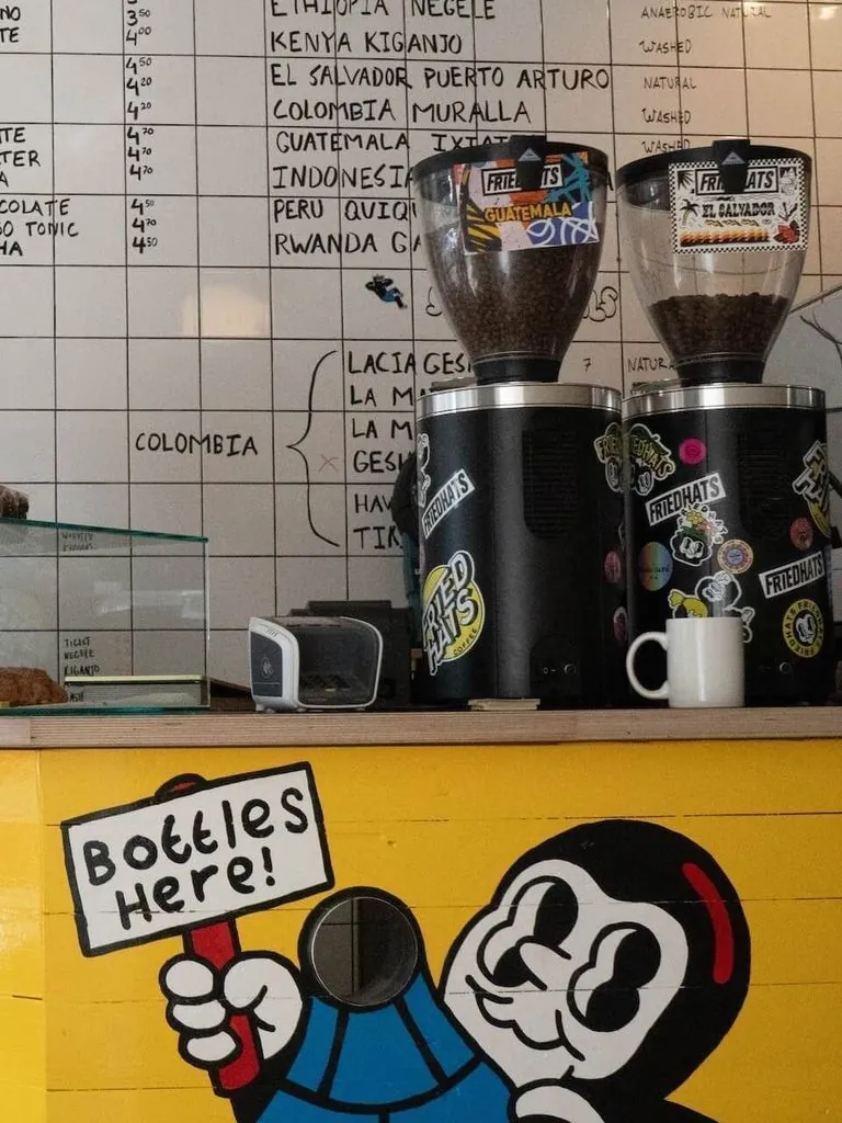 The counter at FUKU, with a chalk menu of single origins, two grinders covered in Friedhats stickers and a cartoon mural on the yellow bar