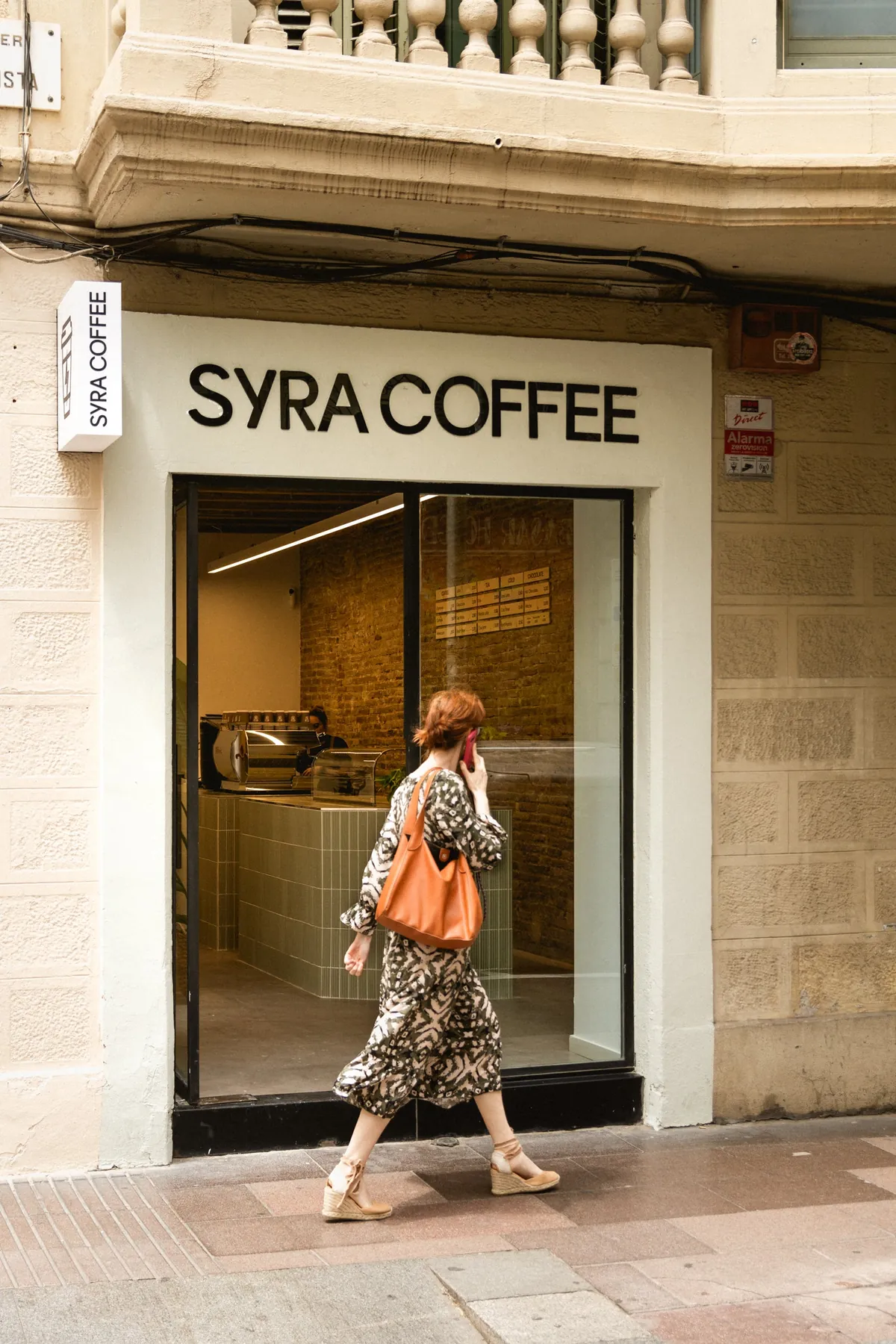 The white Syra Coffee shopfront in Gràcia, with the brick-walled interior visible through the glass