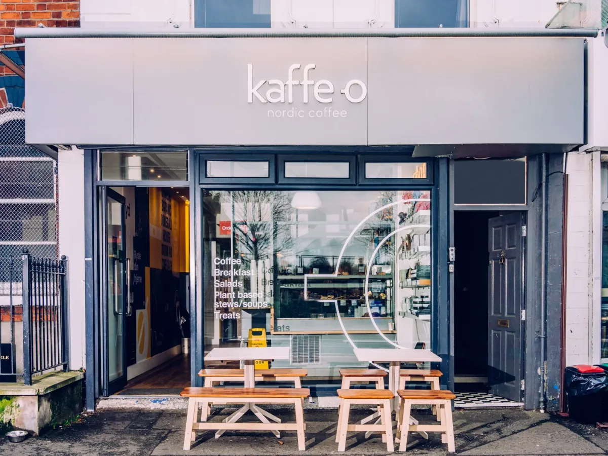 The grey shopfront of a Kaffe O café in Belfast, with the kaffe-o nordic coffee sign and wooden benches on the pavement