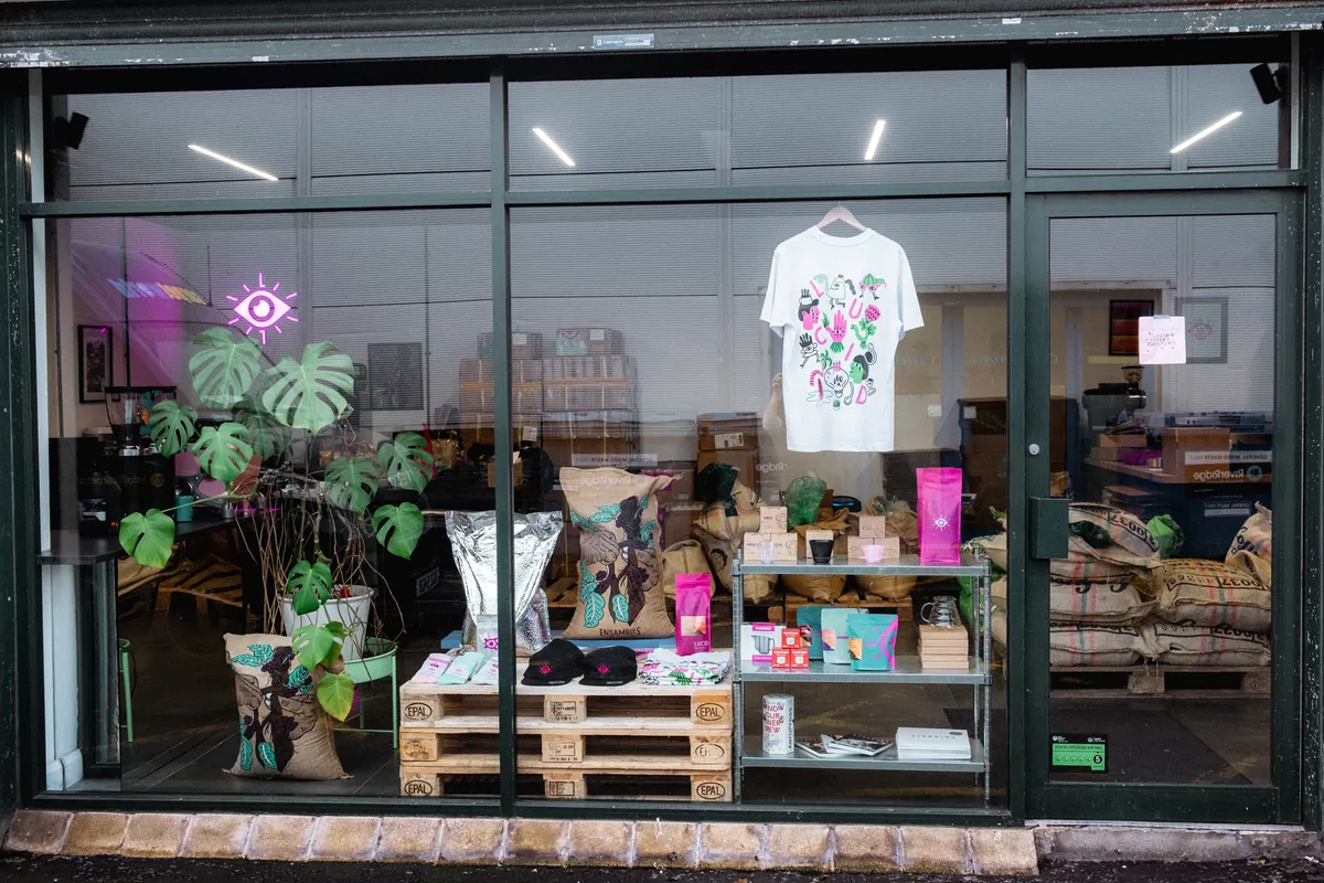 The shop window of the Lucid Coffee Roasters roastery in Belfast, with coffee sacks, retail bags and a neon eye sign inside