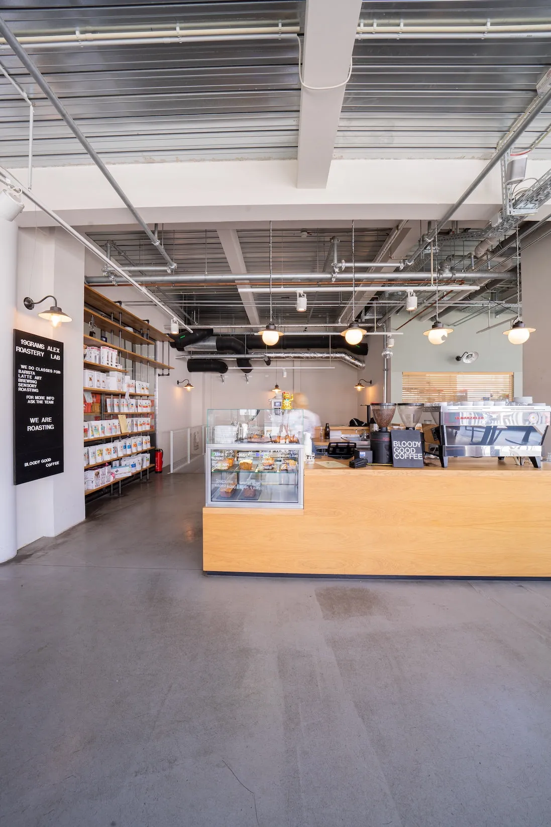The 19grams Alex roastery café, with a long birch counter, pastry case and a sign reading we are roasting