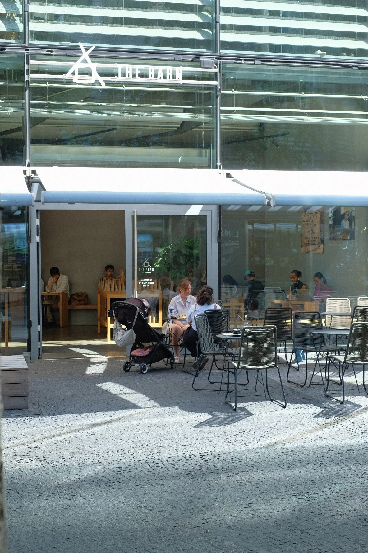 The glass-fronted THE BARN café at the Kranzler Eck, with customers at outdoor tables under the awning