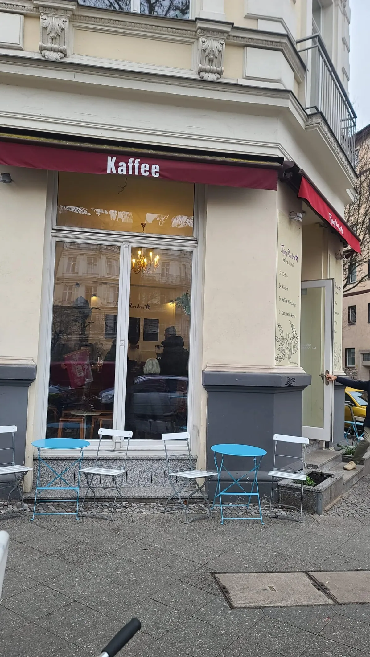 The Flying Roasters café in Kreuzberg, with a red Kaffee awning and blue folding tables on the pavement