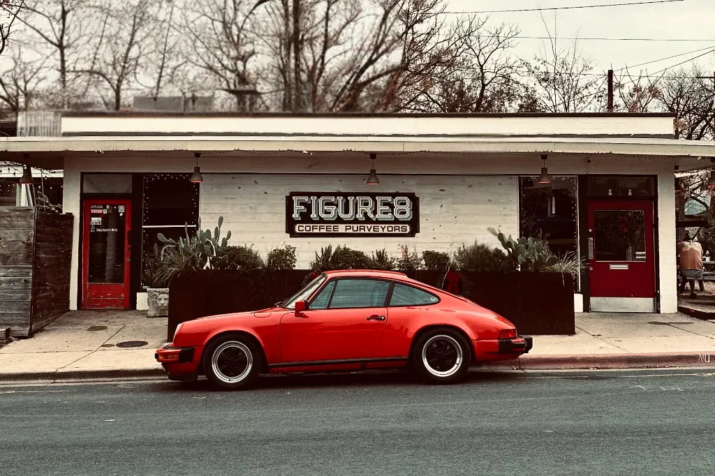 The white Figure 8 café and roastery in East Austin, with a red sports car parked at the kerb