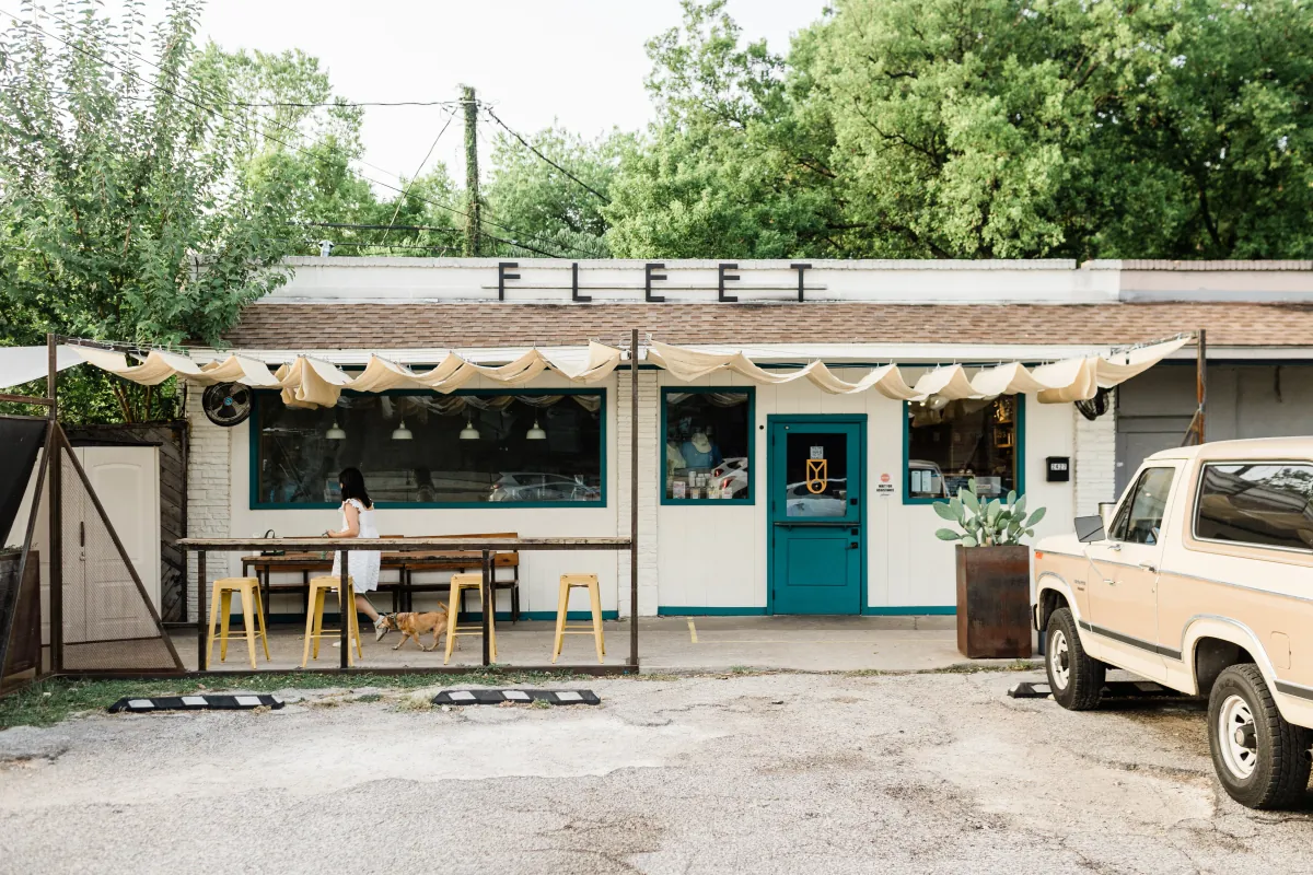 The original Fleet Coffee in East Austin, a low building with a FLEET sign, tables under a pergola and a pickup truck parked outside