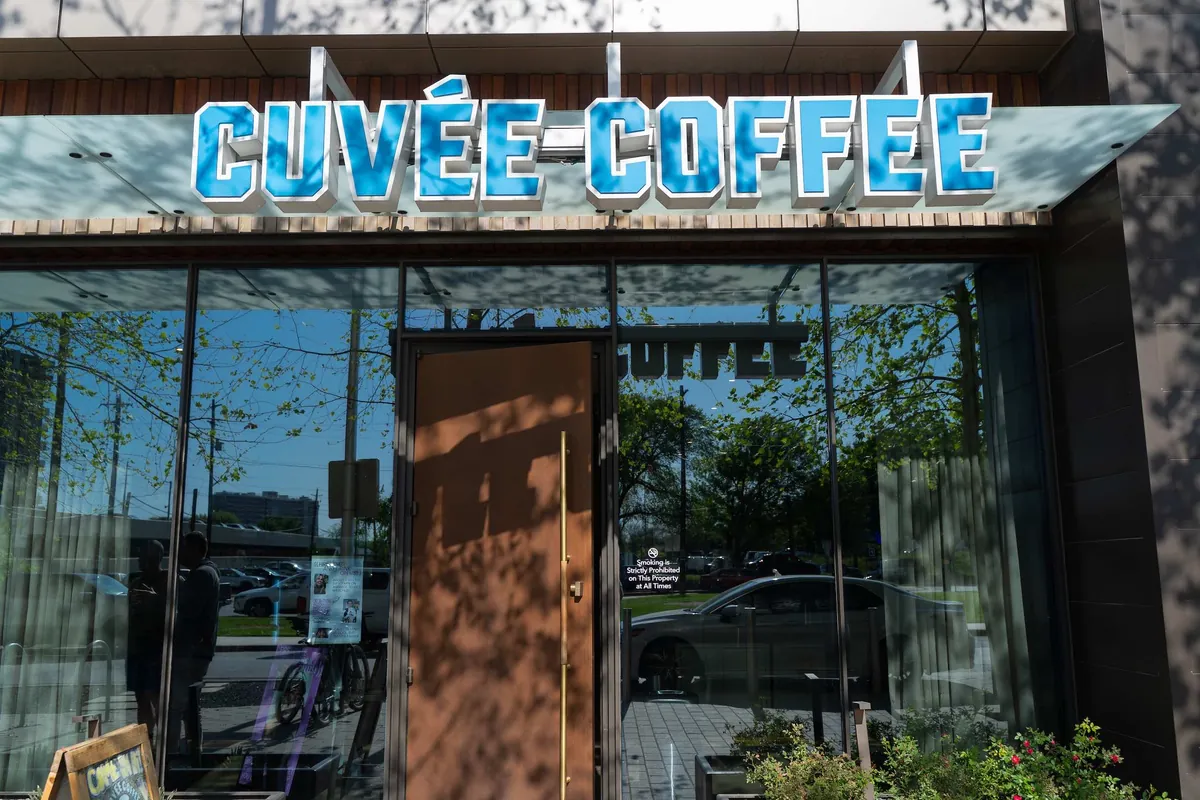 A blue Cuvée Coffee sign above the glass doors of a Cuvée coffee bar