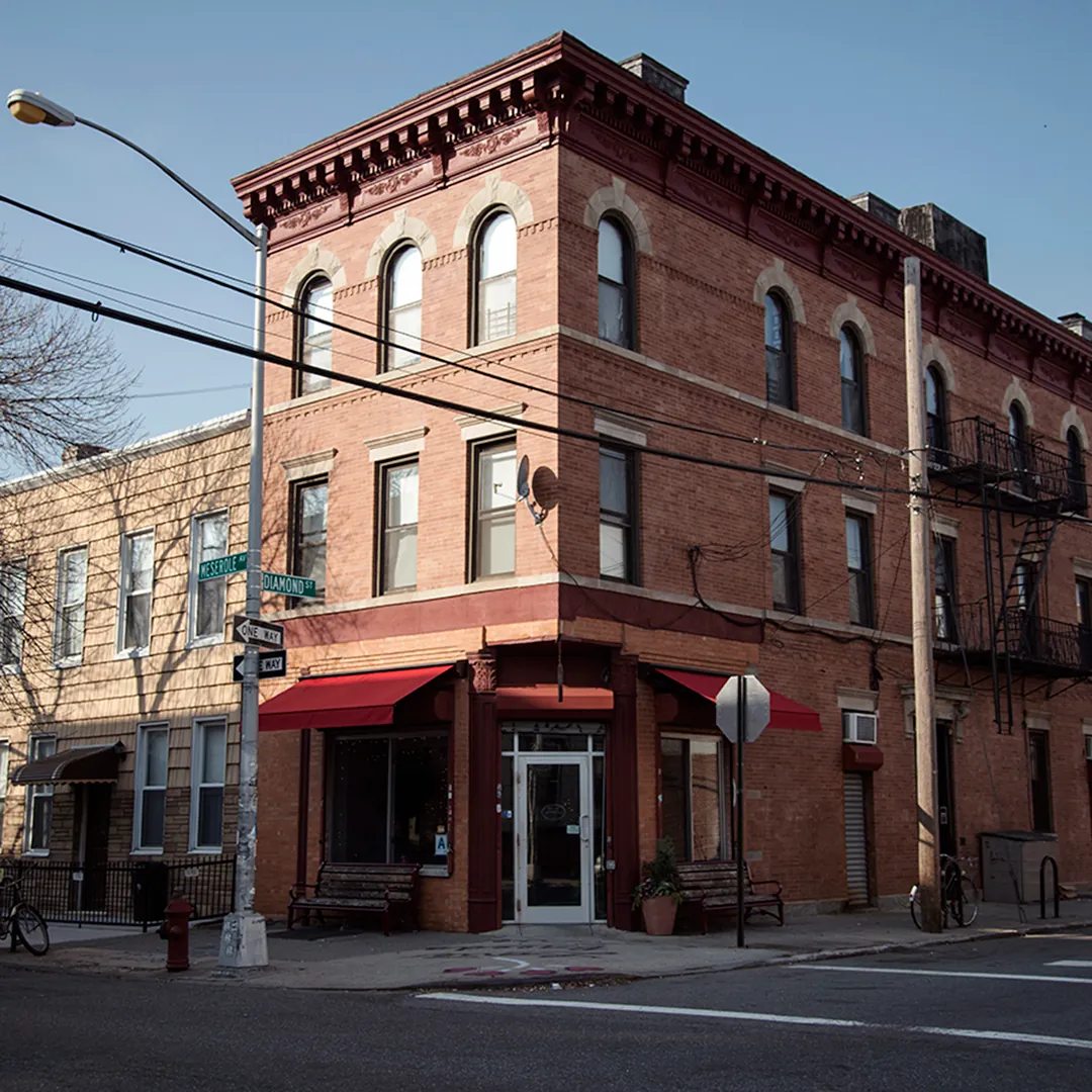 The red-brick corner building of Café Grumpy in Greenpoint, with red awnings over the shopfront and benches on the pavement at the corner of Meserole Avenue