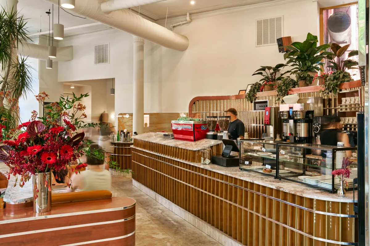 A curved marble-topped counter with fluted wooden panelling at a Variety café, a red espresso machine and grinders at one end and red flowers in a vase in the foreground