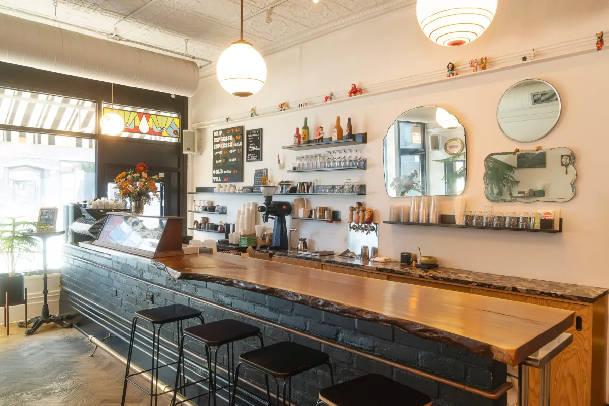 The bar at Four Letter Word in Logan Square, a black-tiled counter with a wooden top, bar stools, round mirrors and white pendant lamps