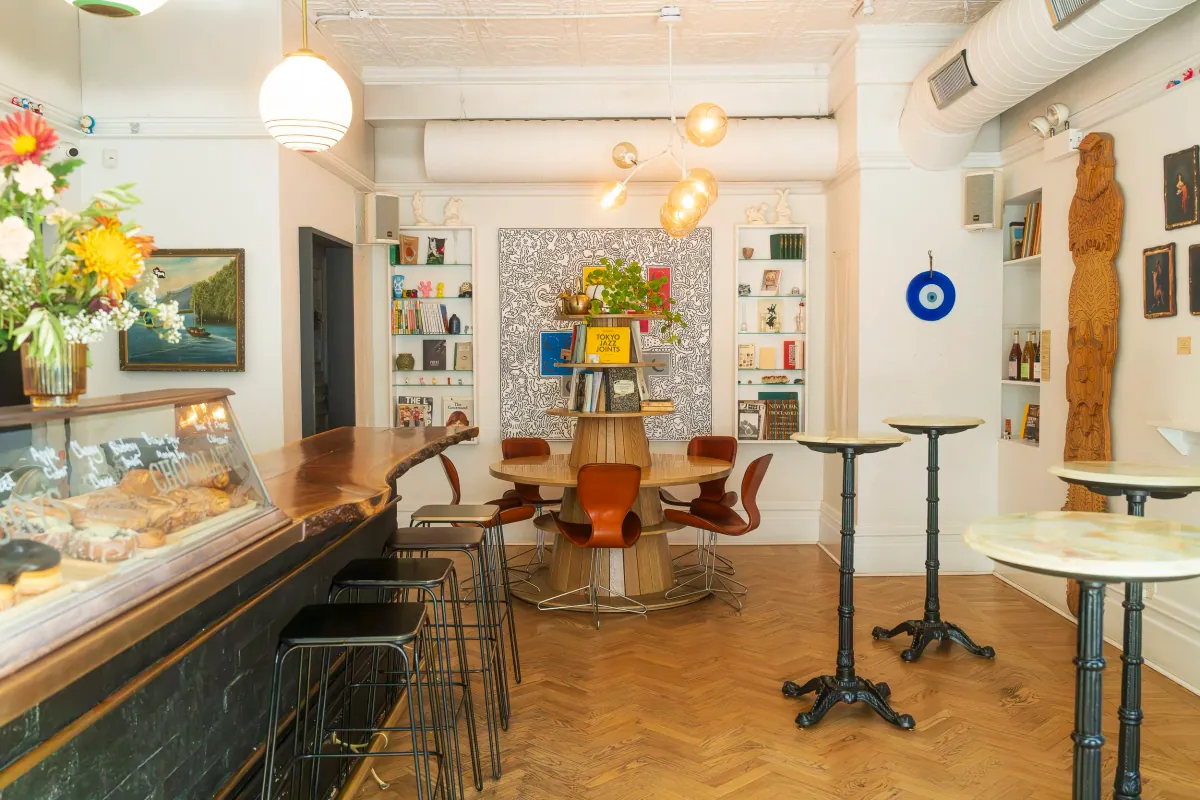 The seating area at Four Letter Word in Logan Square, with a herringbone wooden floor, a round table and marble-topped bar tables under globe pendant lamps