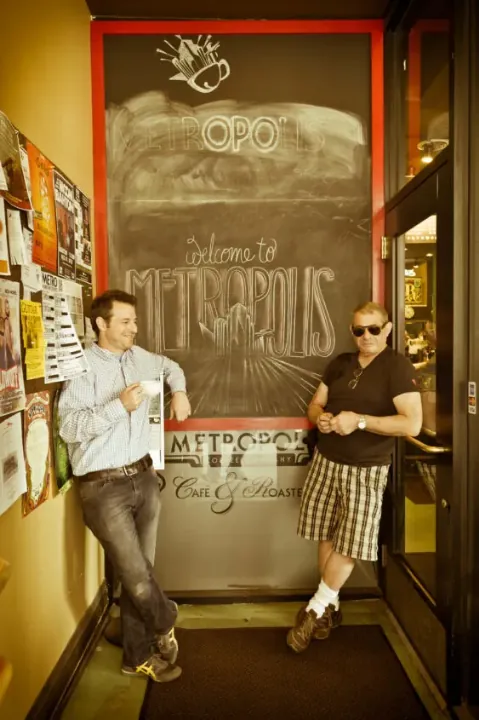 Jeff and Tony Dreyfuss leaning in the doorway of the Metropolis café beside a chalkboard welcome sign