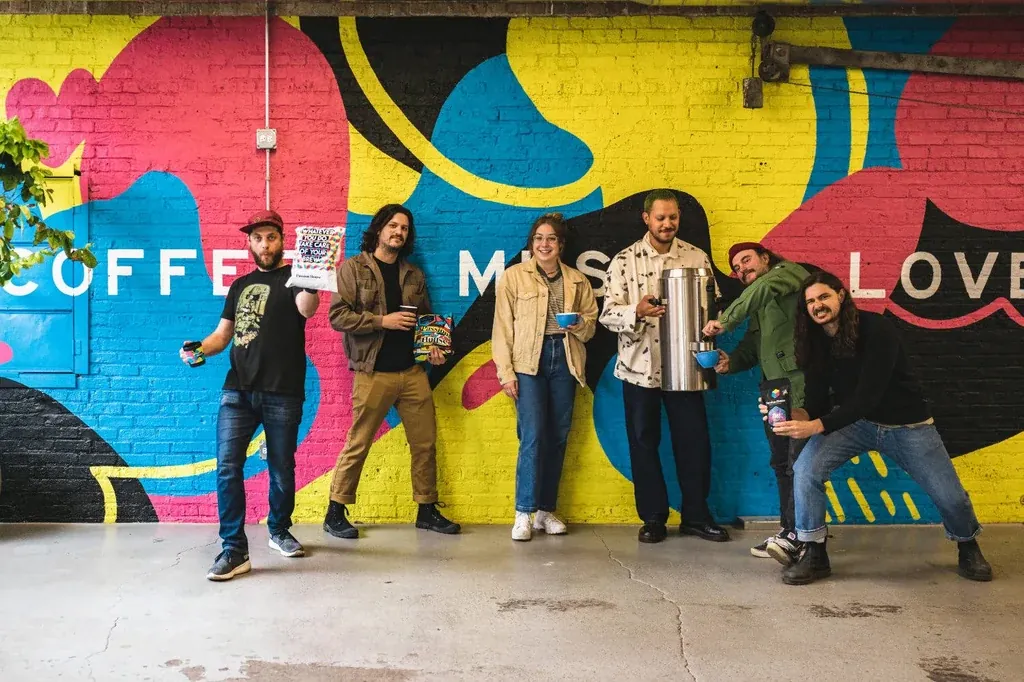 The Passion House team posing in front of a brick wall painted with a colourful mural reading Coffee Music Love