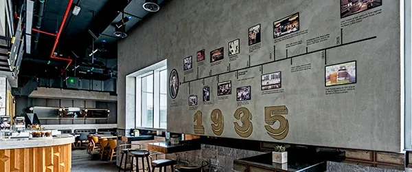 The grey timeline wall at Black Coffee's Duja Tower café, hung with framed photographs over the year 1935 in gold, with bar stools and tables by the window
