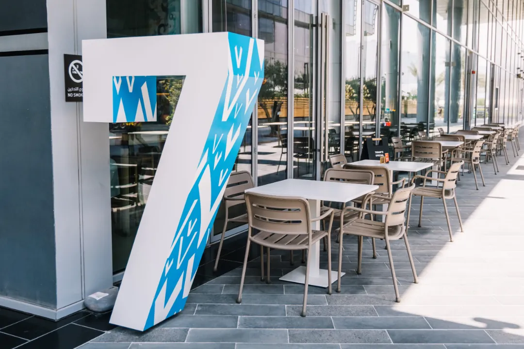 A giant white and blue number 7 standing outside The Espresso Lab’s glass-fronted café in Dubai Design District, beside rows of outdoor tables and chairs