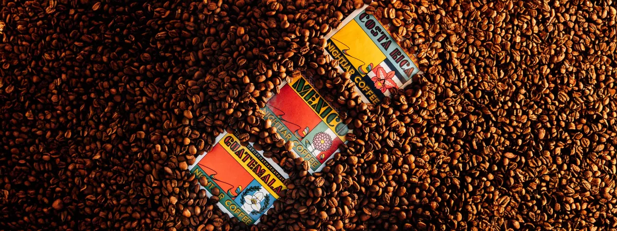 Three Nightjar single-origin bags, Guatemala, Mexico and Costa Rica, lying on a bed of roasted coffee beans