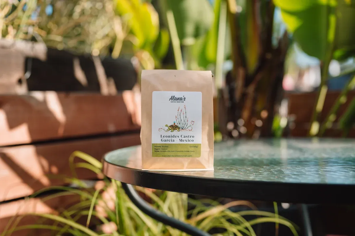 A bag of Alana’s Coffee Roasters coffee on a glass patio table among tropical plants