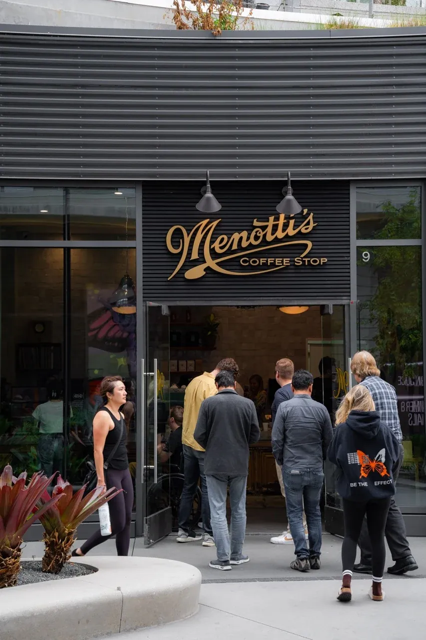 Customers queue at the open door of Menotti’s West LA under its gold script sign
