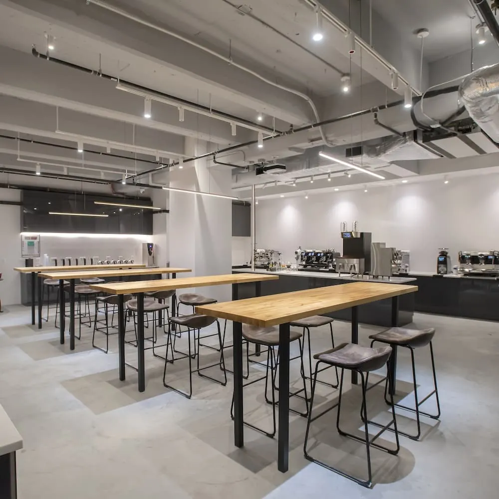 The training lab at Coffee Project New York's Academy, with wooden high tables and stools facing a long counter of espresso machines and grinders