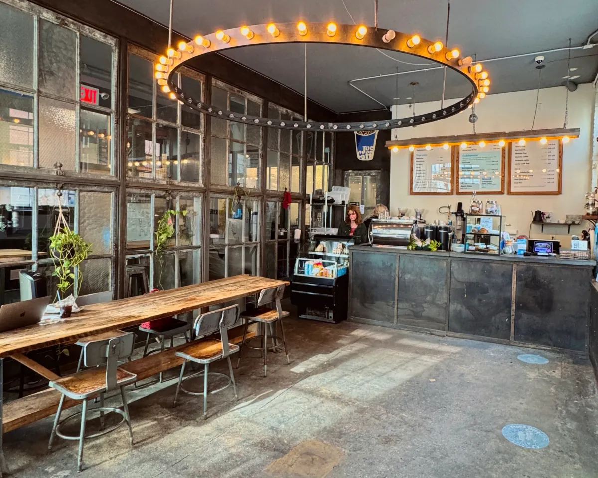 The Long Island City roastery café of Joe Coffee, with a ring of bare bulbs over a long wooden communal table, steel-framed windows and the counter at the back
