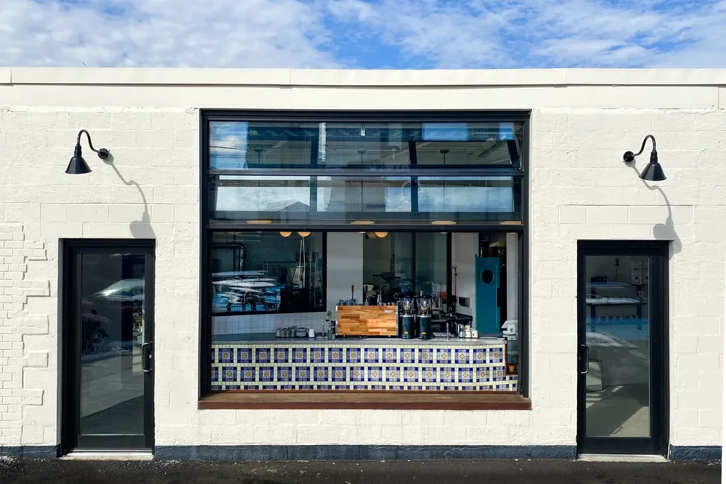 The white-painted brick front of the Ninth Street Espresso roastery and café in Long Island City, with a wide window onto the bar’s blue and yellow tiled counter