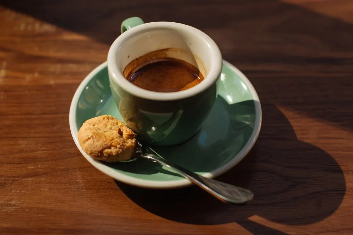 An espresso in a green cup and saucer with a small biscuit and a spoon on a wooden table at Little Collins