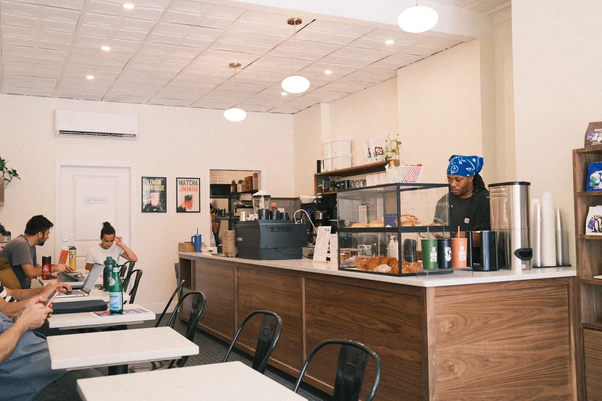 A ReAnimator café with a walnut counter, a pastry case and a barista in a blue bandana under a white pressed-tin ceiling, with guests at marble tables