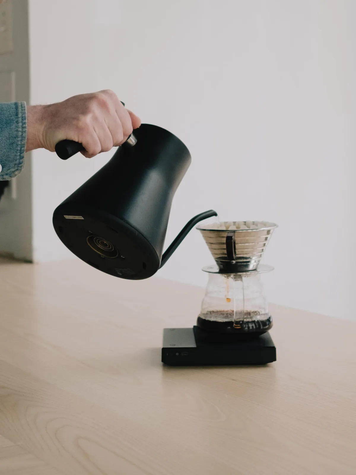 A hand pouring a black gooseneck kettle over a pour-over dripper on a scale at Thank You Thank You
