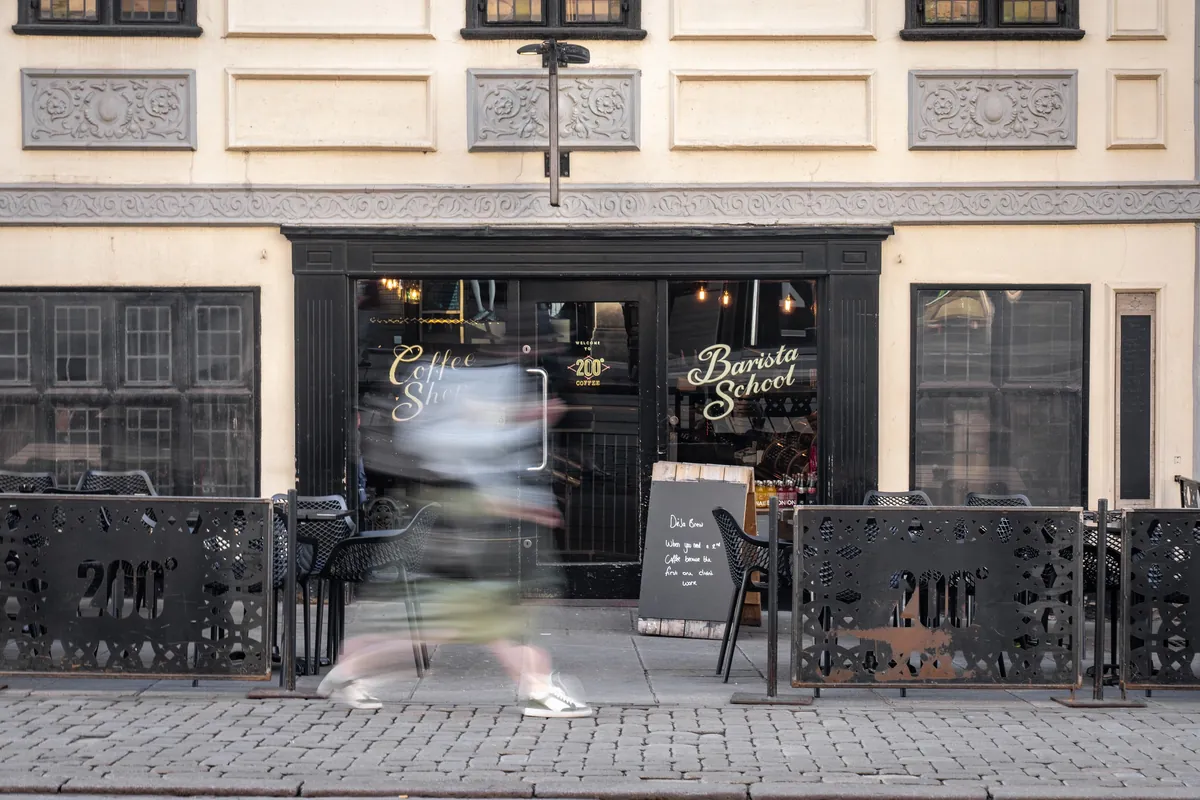 The black shopfront of 200 Degrees in Flying Horse Walk, Nottingham, with Coffee Shop and Barista School painted on the windows and 200° screens around the outdoor tables