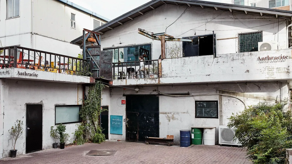 The courtyard of Anthracite Hapjeong, a weathered two-storey former shoe factory with a terrace, black doors and the Anthracite name on the walls
