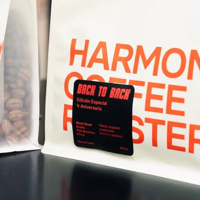 A white Harmony Coffee Roasters bag with Back to Back's red first-anniversary label, Edición Especial 1r Aniversario, beside a glass jar of coffee beans