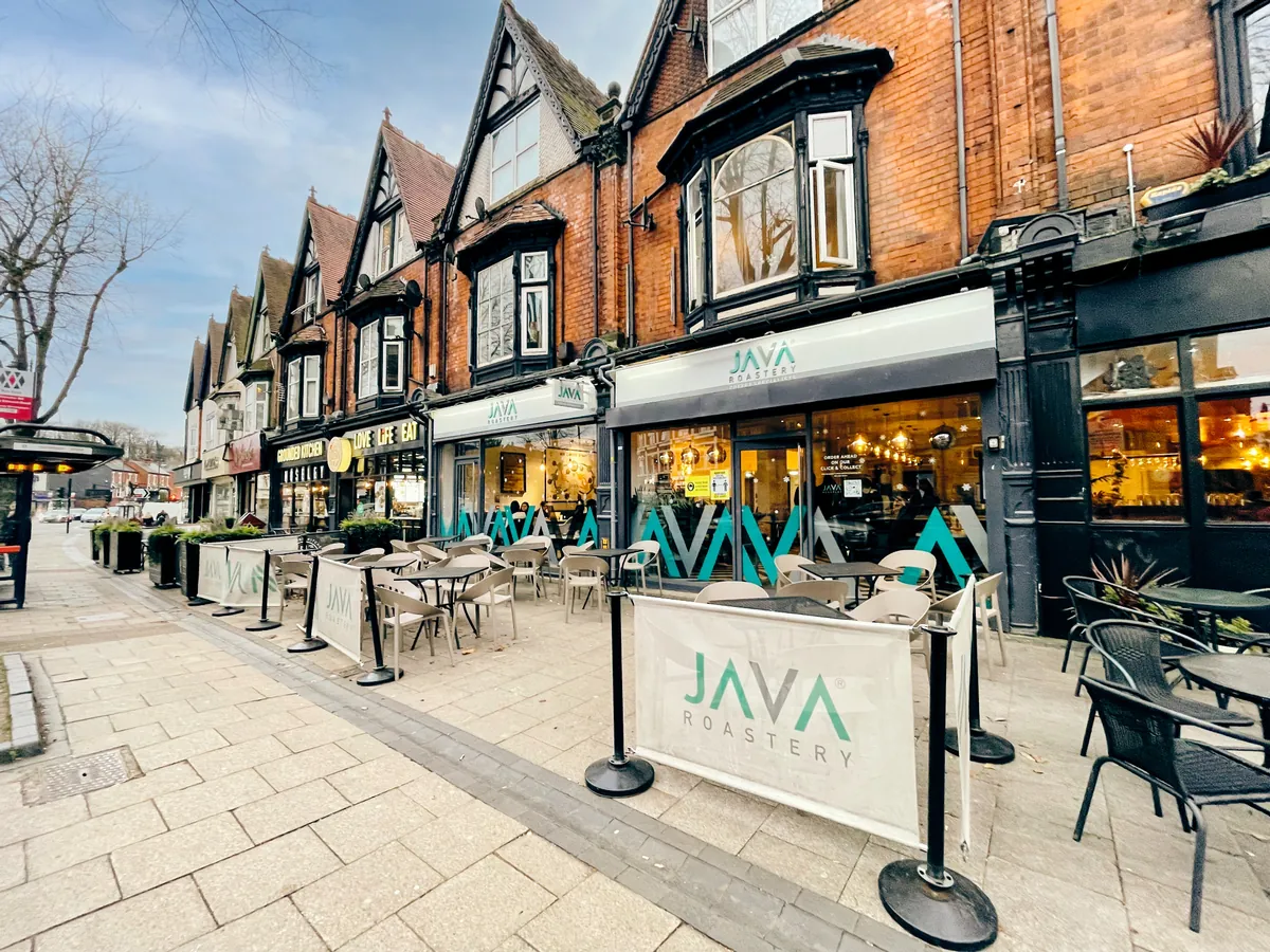 The Java Roastery coffeehouse in Moseley Village, a row of gabled red-brick shopfronts with tables and chairs set out on the wide pavement