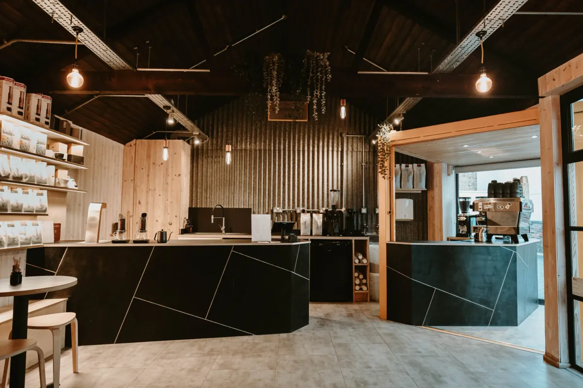 The pale wood and dark counters inside The Scandinavian Coffee Pod in Cheltenham, with shelves of coffee bags, brewing gear on the bar and a second espresso station through a wooden frame on the right