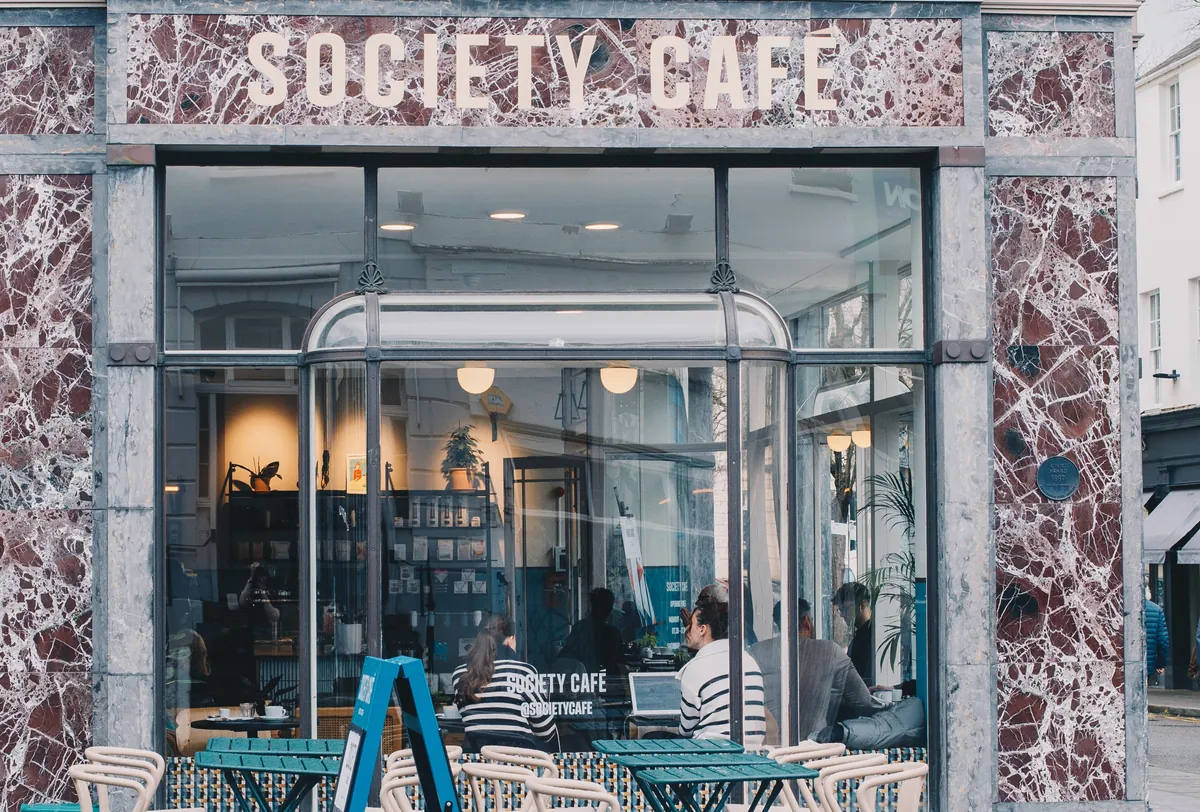 The marble-clad shopfront of Society Café in Cheltenham, with the café name above tall windows and tables on the pavement outside