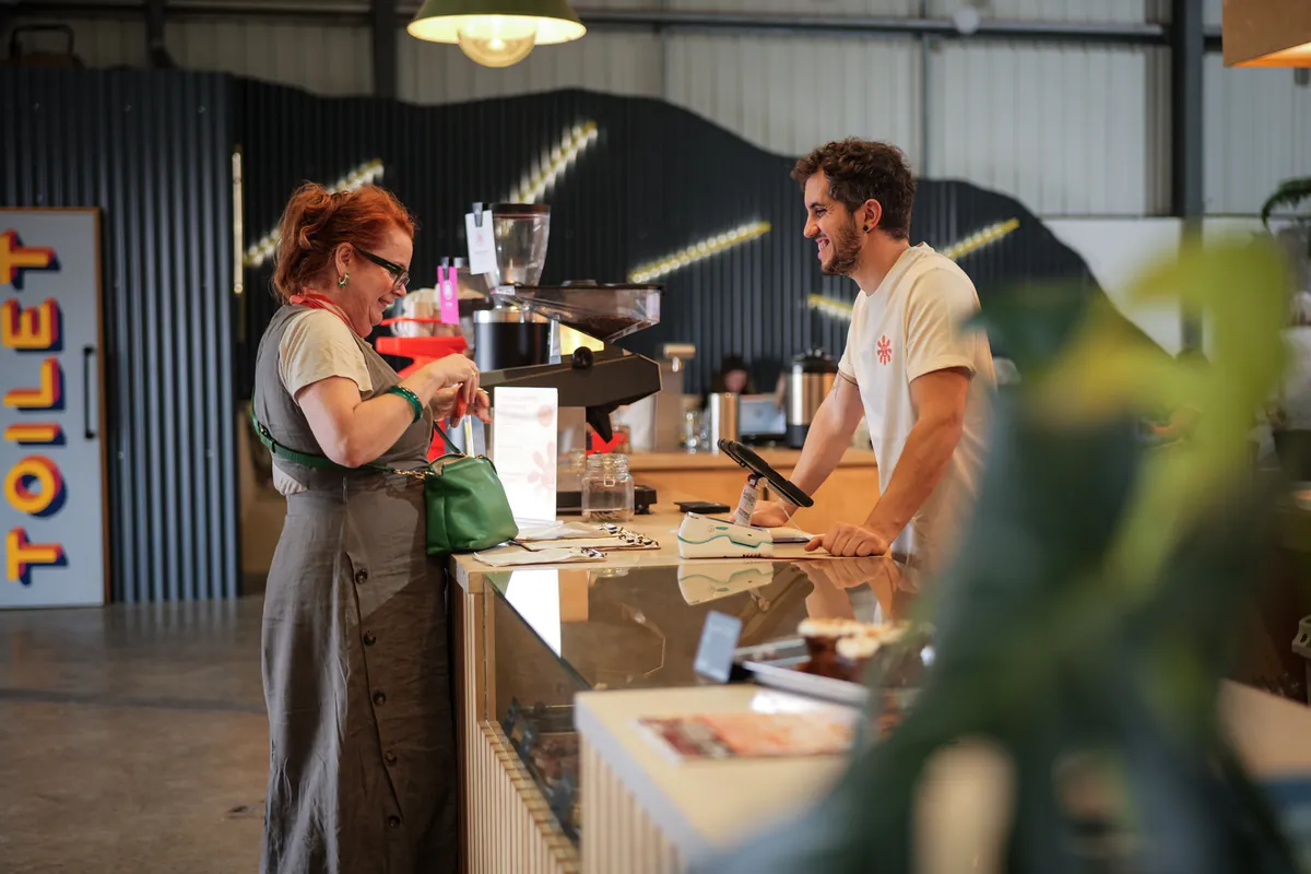 A customer pays at the counter of the Ritual brew bar in Cheltenham while a barista smiles behind the till, with the espresso machine and grinders on the back bar