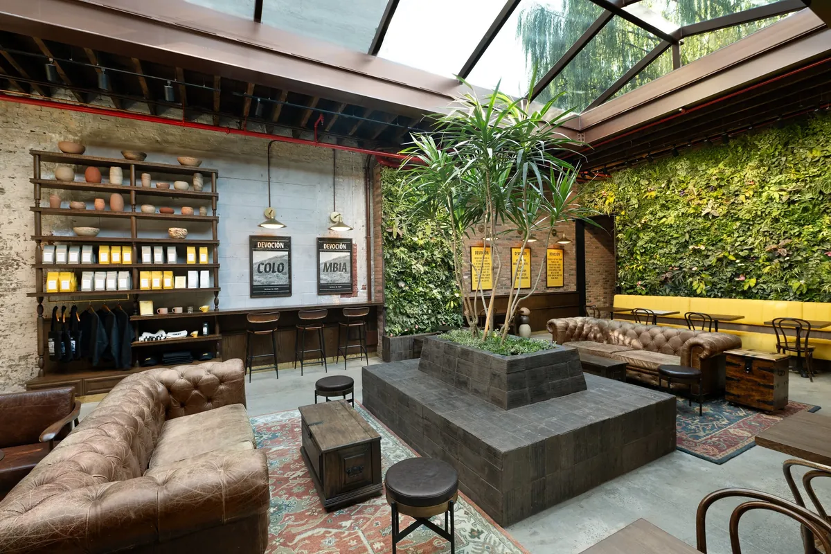 Leather sofas, a raised planter with a palm tree and a living green wall under the glass roof of Devoción in Williamsburg
