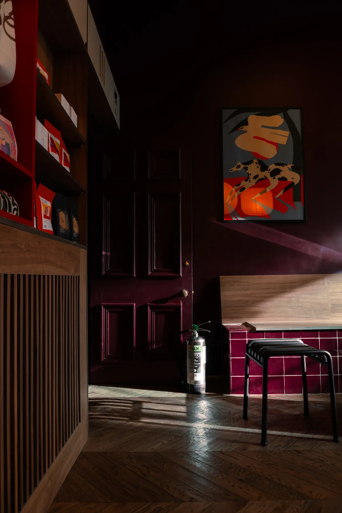 The burgundy-walled interior of Effy in Nottingham, with a wooden bench, a black stool, red shelving and an orange poster beside a panelled door