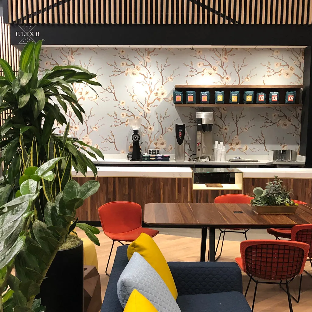 An Elixr café counter with cherry-blossom wallpaper, a shelf of coffee bags and orange chairs around a walnut table