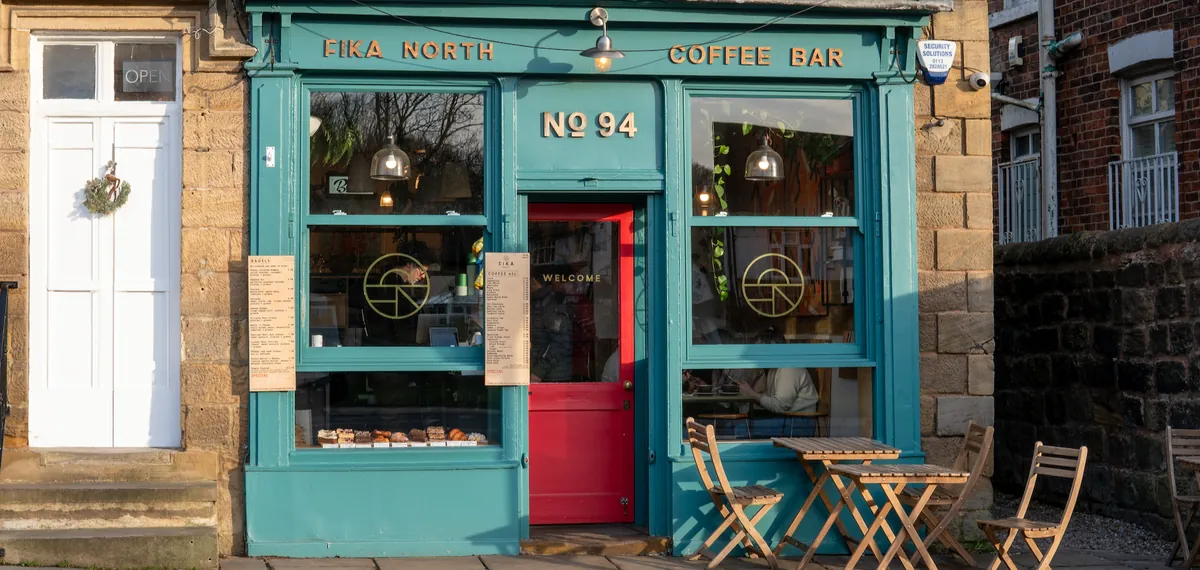 The teal shopfront of Fika North in Far Headingley, Leeds, with a red door, menus in the windows and folding chairs and tables outside