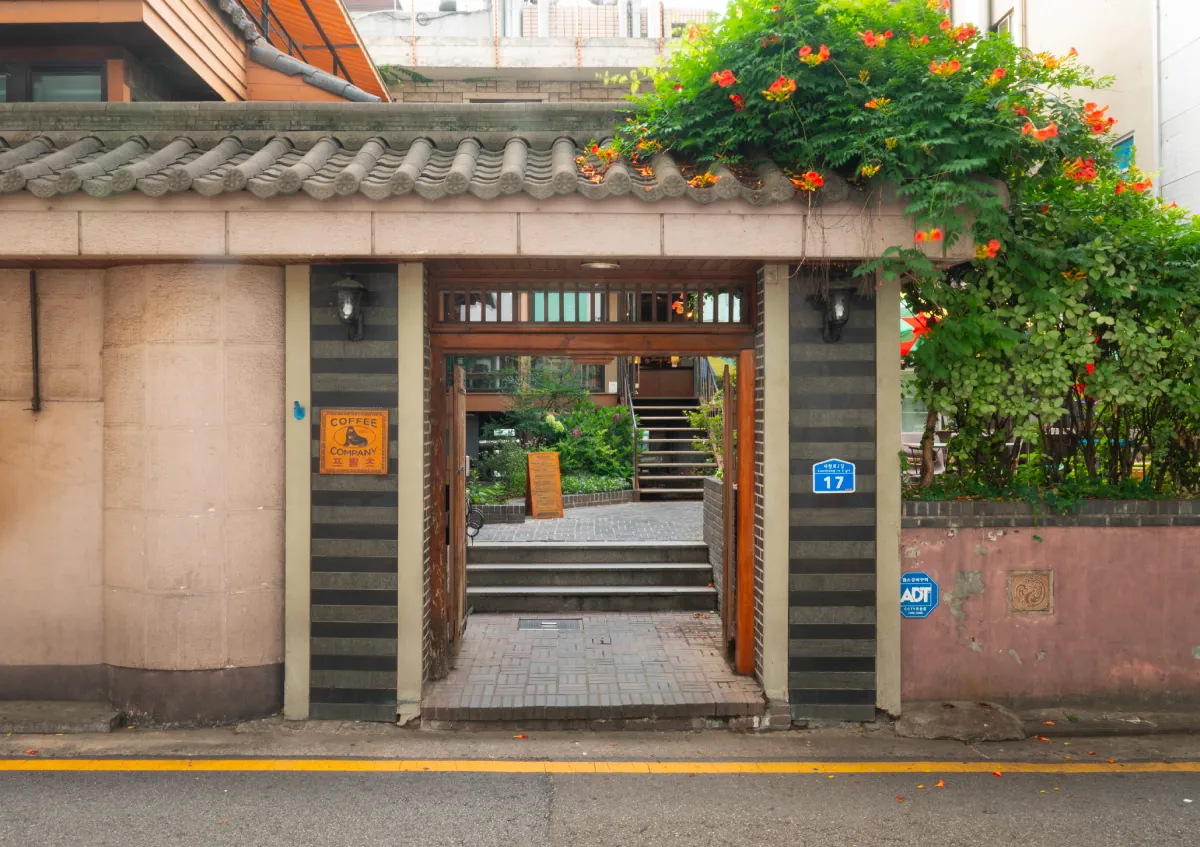 The gated entrance of Fritz Dohwa, under a tiled roof and a flowering vine, with steps leading up to the café