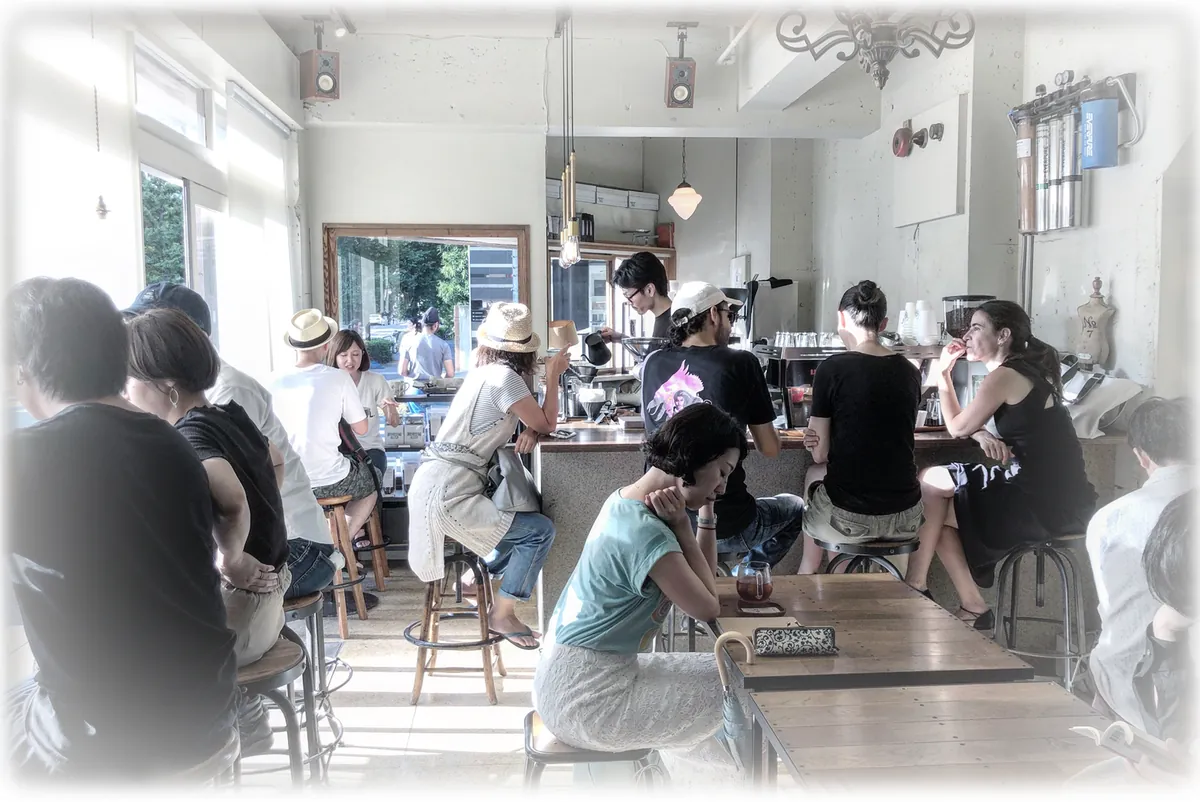 Customers on stools and benches at the counter and long tables of a bright, white-walled GLITCH café, with baristas working behind the bar