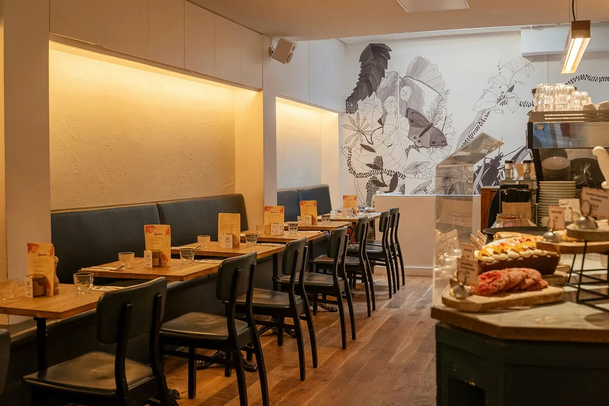 Banquette tables beneath a black-and-white botanical mural, with the pastry counter in the foreground, upstairs at Lantana Fitzrovia