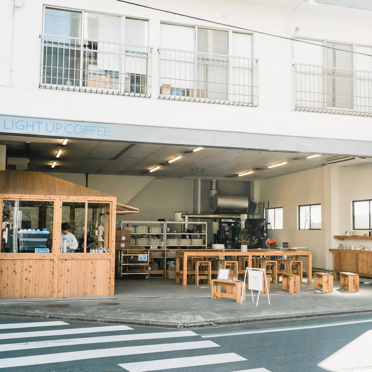 The open front of the LIGHT UP COFFEE roastery café in Mitaka, a former car factory with a timber counter booth, long wooden tables and the roaster at the back