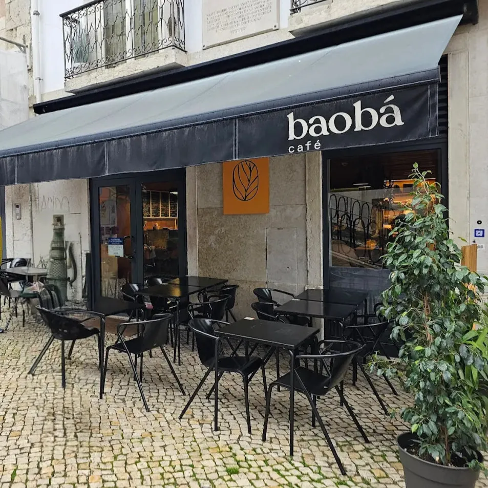 The terrace of a Baobá café in Lisbon, with black tables and chairs on cobblestones under a dark awning lettered baobá café