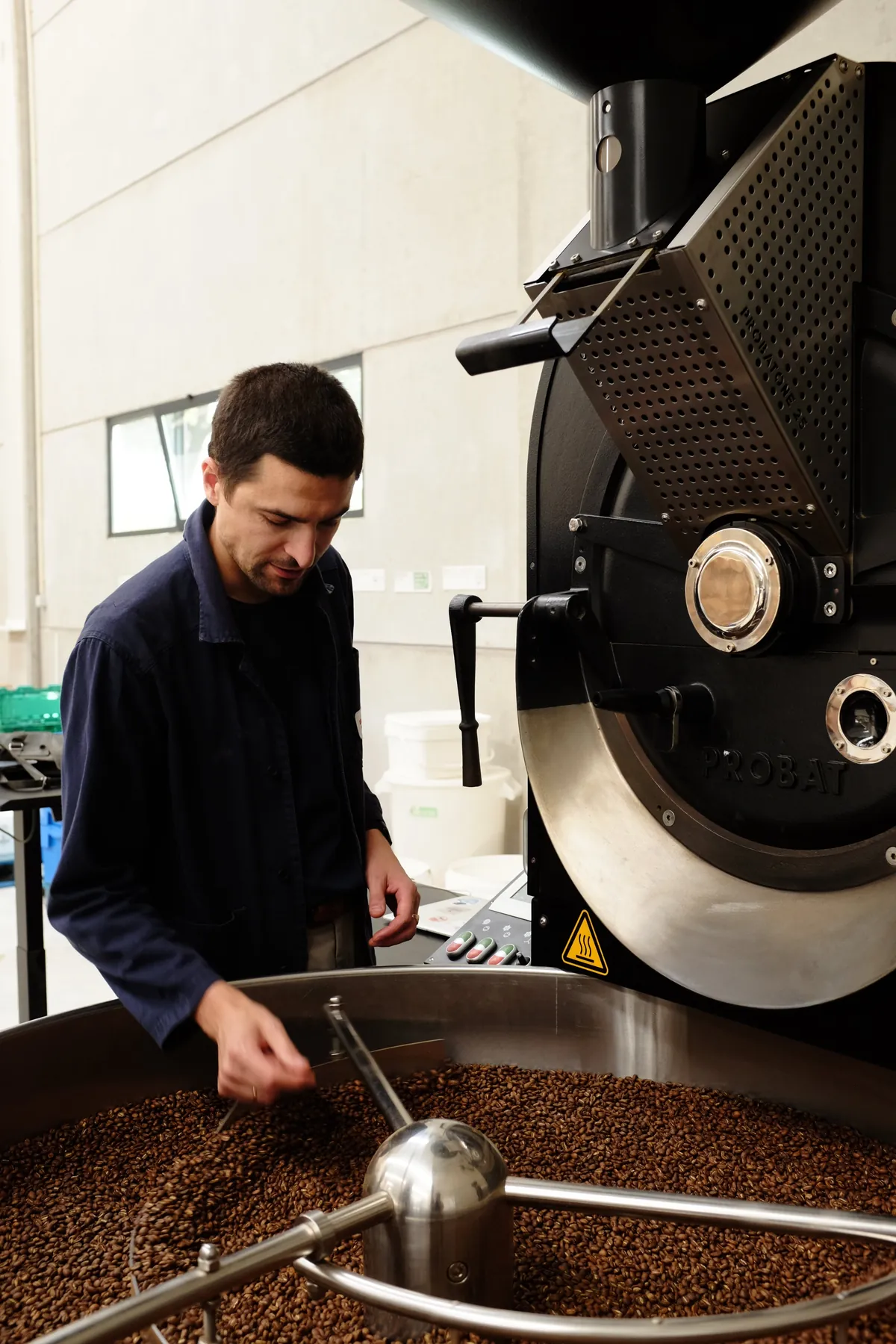 A roaster checks freshly roasted beans turning in the cooling tray of a black Probat roaster at Fábrica Coffee Roasters