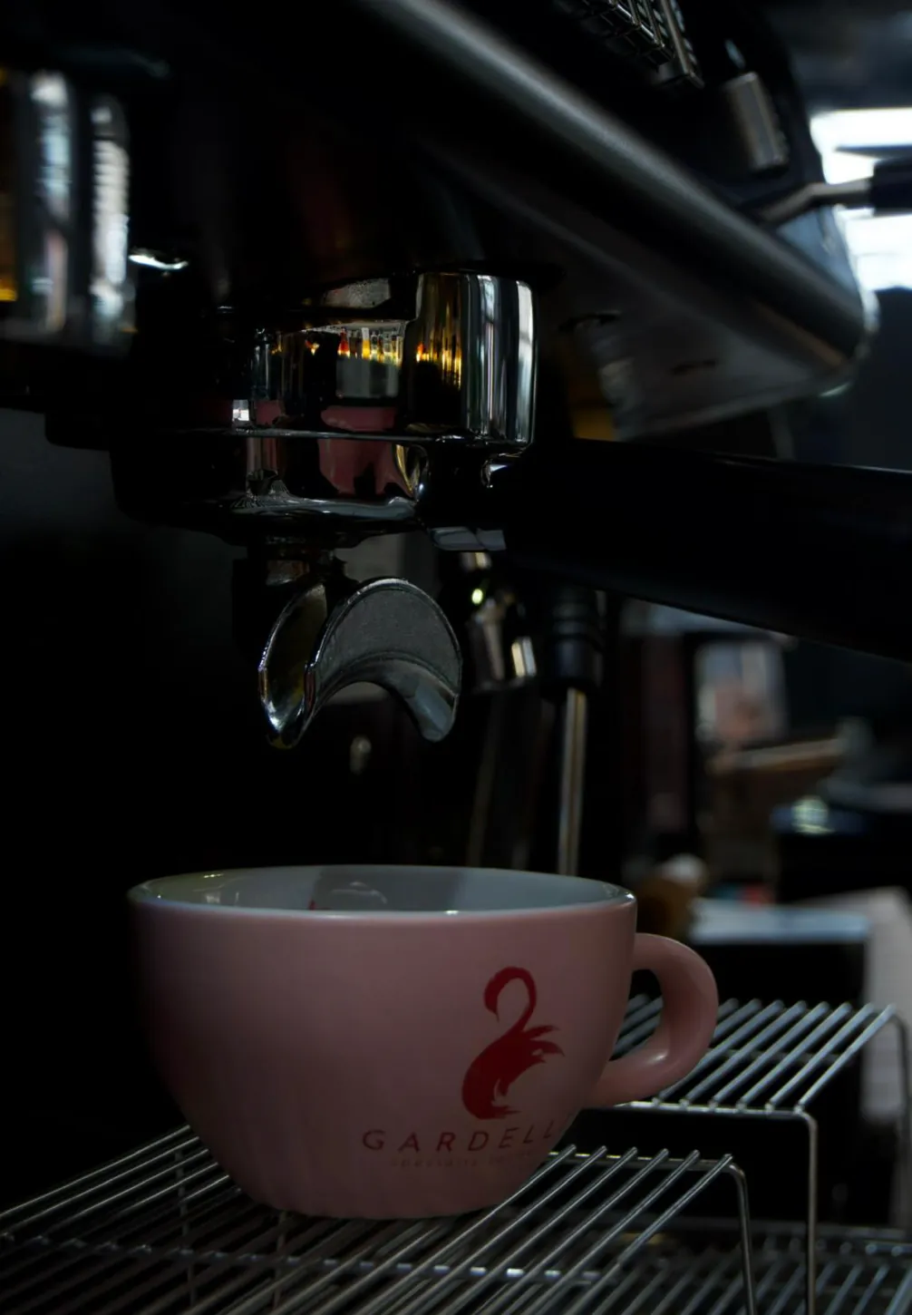 An espresso pours from the group head into a pink Gardelli cup on the drip tray of the espresso machine