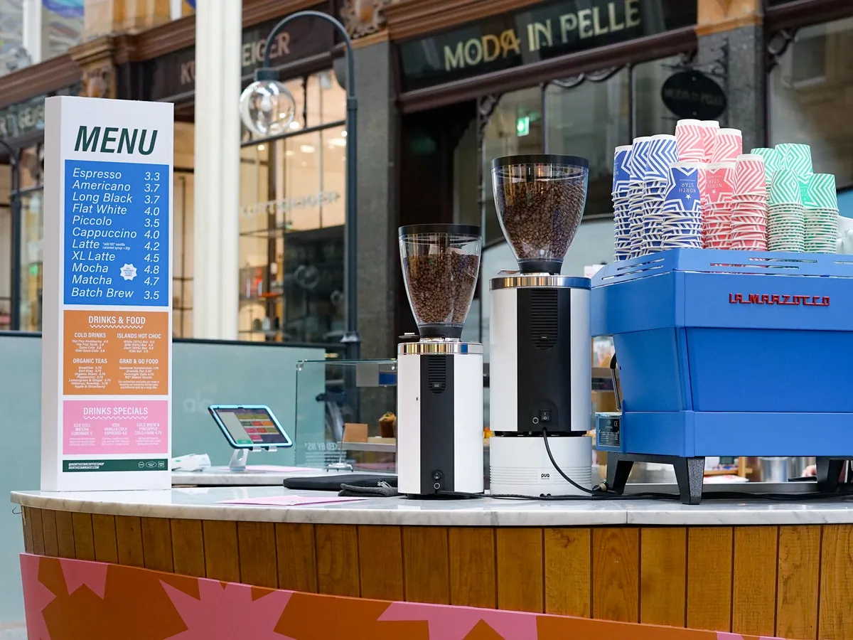 The North Star kiosk in Leeds' Victoria Quarter, with a menu board, two grinders and a blue espresso machine on a patterned counter under the arcade
