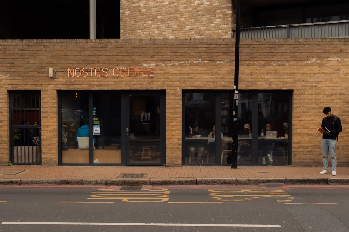 The brick shopfront of Nostos Coffee in Battersea, with its name in orange neon above the windows