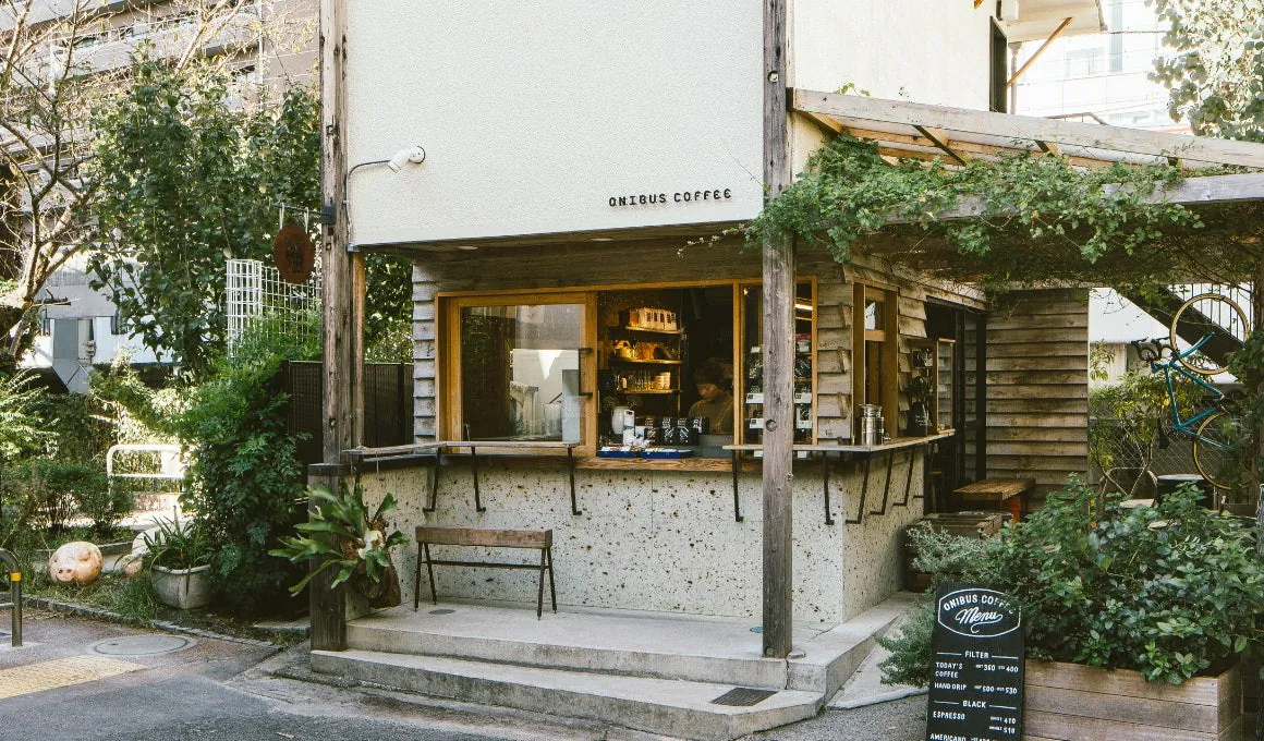 The ONIBUS COFFEE stand by Nakameguro station, a small white building with a wooden service window, a bench and potted plants