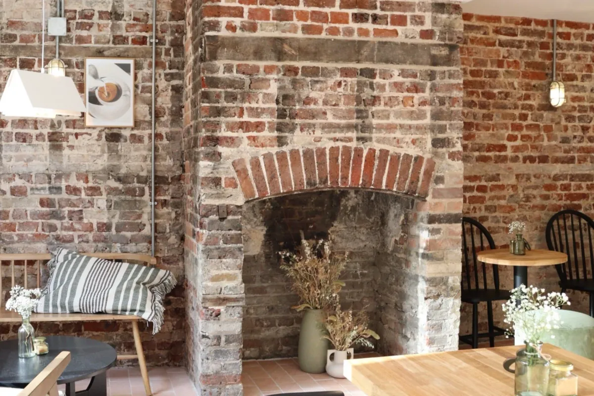 Inside Pages Coffee House in Cambridge: exposed brick, an old brick fireplace, a cushioned bench and wooden tables with dried flowers