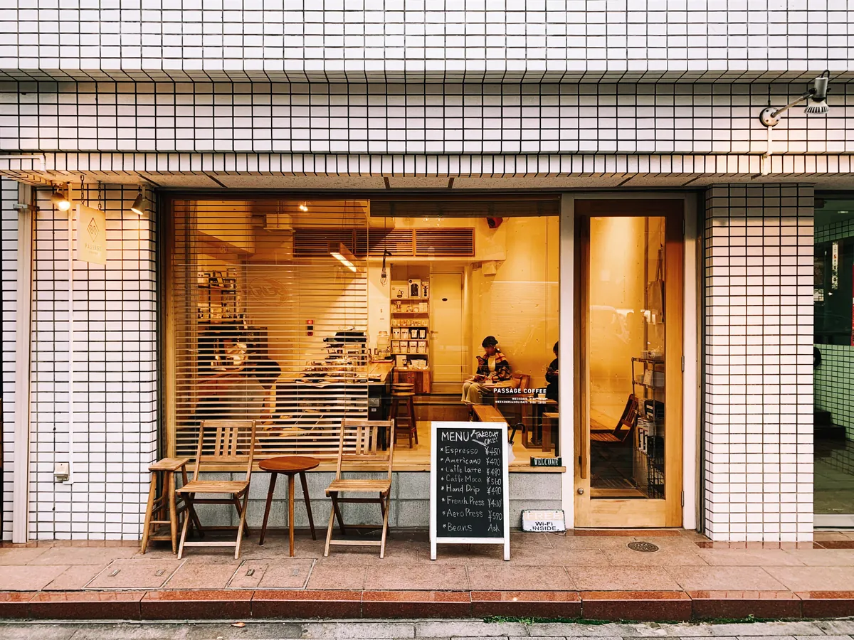 A PASSAGE COFFEE shop front of white tiles and glass, with wooden chairs and a chalkboard menu on the pavement